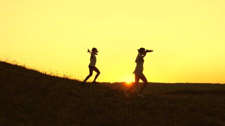 Dreams of flying. Happy childhood concept. Two girls play with a toy plane at sunset. Children on background of sun with an airplane in hand. Silhouette of children playing on planeの写真素材