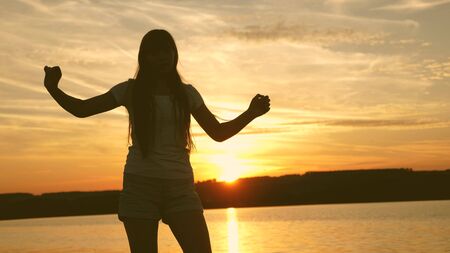 young woman dancing at sunset party. Free and cheerful woman. Happy girl with long hair is dancing at sunset on the beach and laughing. Slow motion.の写真素材