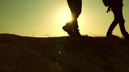 teamwork business people. feet of Free Travelers adventurers walk along top of the mountain in rays...