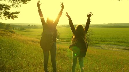 Hiker Girls teamwork. free traveler girls raise their hands up, celebrating victory and enjoying scenery, in sun. happy women on vacation travel through woods with backpack, raise their hands up.の写真素材