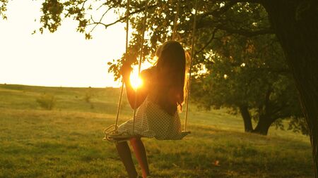child swinging on a swing in park in sun. teen girl enjoys flight on swing on summer evening in forest. concept of happy family and childhood.の写真素材