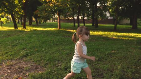 baby plays in park in spring. Slow motion. kid plays on the lawn in the summer. Happy child runs on a meadow in summer on a green grass. cheerful little girl runs across field. concept of happiness.の写真素材
