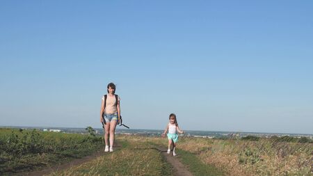 Travelers mother with a child walk on road. Mom and little daughter travel out of town. joyful kid runs along the road. concept of happy childhood and family.の写真素材
