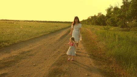 Mother and baby rest in park. concept of a happy childhood. little daughter and mom walk along road past field. child plays running away from mom. happy family with child walks in countryside.の写真素材