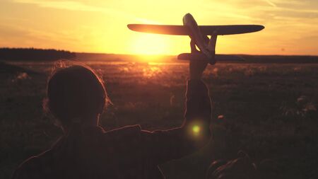 Happy girl runs with a toy airplane on a field in the sunset light. children play toy airplane. teenager dreams of flying and becoming pilot. the girl wants to become pilot and astronaut. Slow motionの写真素材