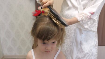 mother combs the childs hair with a comb. concept of beautiful hairstyle for daughter. a happy family. Mom Braids the Braid Of Her Little Daughter.の写真素材