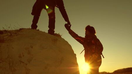 team of climbers climbs a mountain holding out a helping hand to each other. Free woman traveler climb mountain. teamwork of tourists. Travel and adventure in mountains at sunset.の写真素材