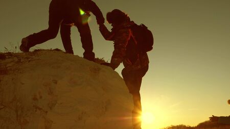 team of climbers climbs a mountain holding out a helping hand to each other. Free woman traveler climb mountain. teamwork of tourists. Travel and adventure in mountains at sunset.の写真素材