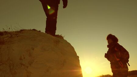 team of climbers climbs a mountain holding out a helping hand to each other. Free woman traveler climb mountain. teamwork of tourists. Travel and adventure in mountains at sunset.の写真素材