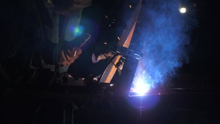 Industrial worker in a protective mask using modern welding machine for welding metal structures in...
