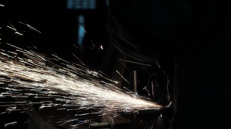a worker at factory processes metal, sparks fly. close-up. Circular saw cuts metal in a workshop. man works on the conqueror. metalworking in a factory.の写真素材