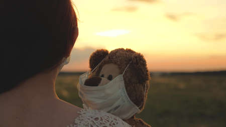 A child holds his beloved teddy bear in a protective maskの写真素材