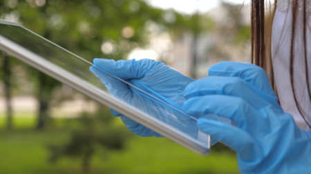 a healthy girl is walking in medical gloves working with a tablet in a city park. close-up. COVID-19. danger of virus. young business woman working remotely on street. Safe and social distance.の写真素材