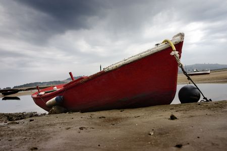 A red and old fishing boat stranded in the sand of a beach near a little fishing rural villageの写真素材