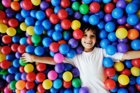 Little smiling boy playing lying in colorful balls park playground