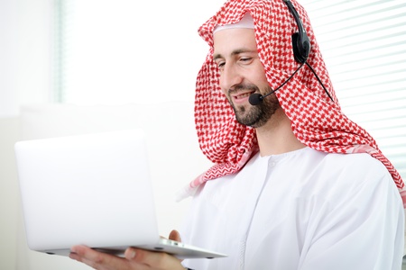 Portrait of a smart arabic business man using laptop and hheadset. Call center. Customer support. Helpdesk.の写真素材