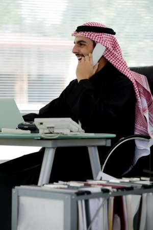 Portrait of a smart arabic business man using laptop and talking  on the phoneの写真素材