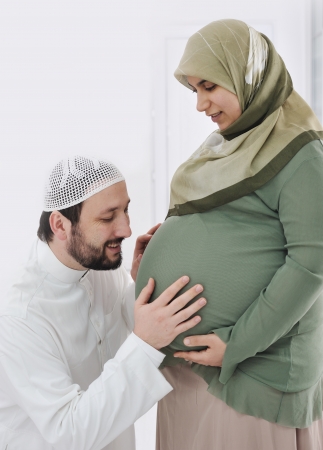 Pregnant  muslim  wife smiling with her  husband kissing belly,and his hands on bellyの写真素材