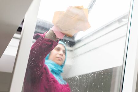 Muslim woman cleaning windows in living room