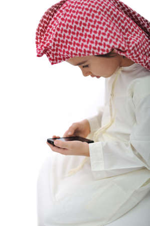 Kid with traditional middle eastern clothes playing typing message on cell phoneの写真素材
