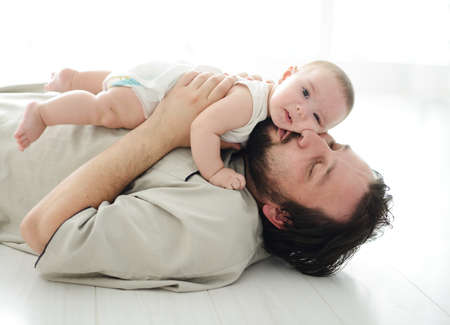 Young father lying on floor at home and playing with adorable baby