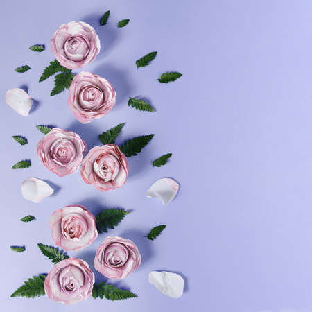 Creative layout made with paper pink rose flowers and petals, and green leaves on bright pastel purple background. Minimal flat lay with copy space. Spring visual.の写真素材