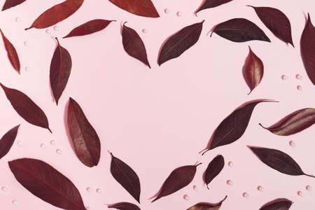 Creative composition with heart shape made of dark red leaves and shiny pearls on pastel pink background. Flat lay. Minimal romantic concept with copy space.の写真素材