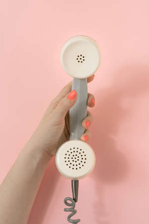 Vintage scene with female hand scrolling retro phone receiver. Minimal composition on pastel pink background. Top view.の写真素材