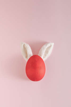 Minimal visual made of red Easter egg with bunny ears on pink background. Creative holiday idea. Flat lay aesthetic.の写真素材