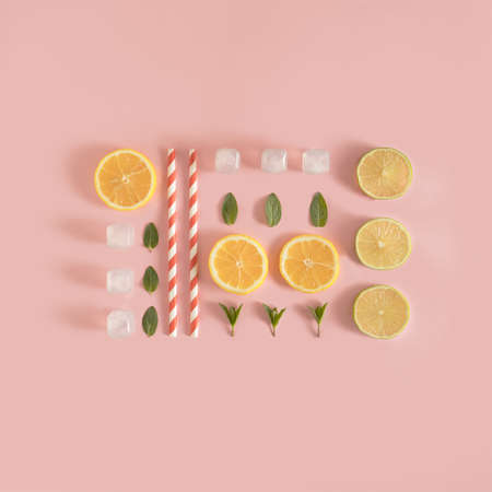 Neatly arranged lemon and lime slices, ice cubes, mint leaves and paper straws on pastel pink background. Creative summer concept. Minimal refreshment idea. Flat lay aesthetic.の写真素材