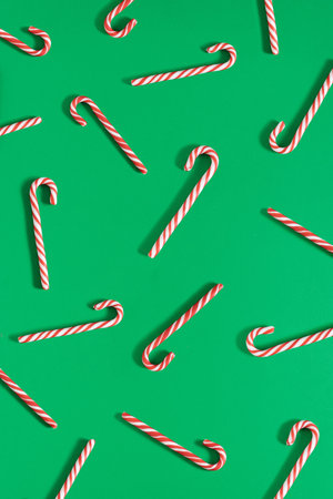 Creative holiday pattern made of red and white striped candy canes on green background. Minimal Christmas spirit aesthetic. New Year flat lay visual.の写真素材