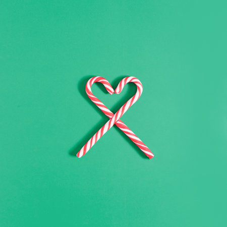 Minimal holiday composition with two candy canes making heart shape on green background. Christmas...