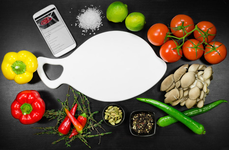 Recipe on display mobile phone with white cutting board among the vegetables. Top viewの写真素材