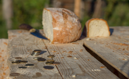 Half a loaf of bread on a table with coins and knife. Part of the image is blurredの写真素材