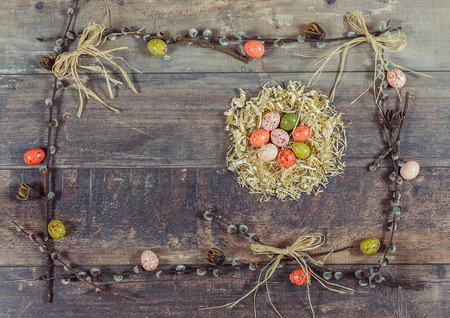 Chocolate colored eggs in the nest of sawdust, decorated frame of pussy-willow, bows of dry grass and seed pods on a background of brown wood.の写真素材