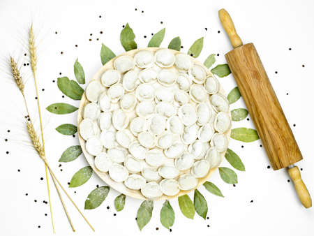 Meat dumplings - russian pelmeni with ears, bay leafs, rolling-pin and bell pepper on white isolated background. Top viewの写真素材