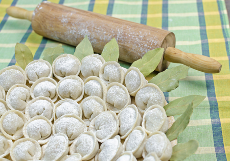 Meat dumplings - russian pelmeni on a round plate with bay leaf and rolling-pin on the green towelの写真素材