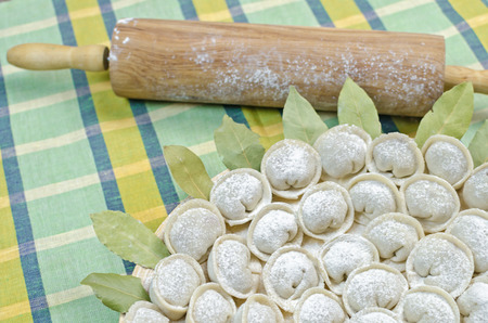 Meat dumplings - russian pelmeni on a round plate with bay leaf and rolling-pin on the green towelの写真素材