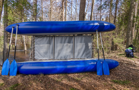 Inflatable blue catamaran with oars is leaning against the trees in the forest.の写真素材