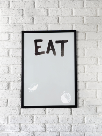 Photo of poster with text Eat in a black frame on a white brick wall. Empty space for text.の写真素材