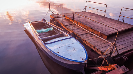 Old rowboat moored wooden pier amazing sunset lake river. Old rowboat prishvartovanaya to a wooden pier on the lake. A beautiful golden sunset on the river.の写真素材