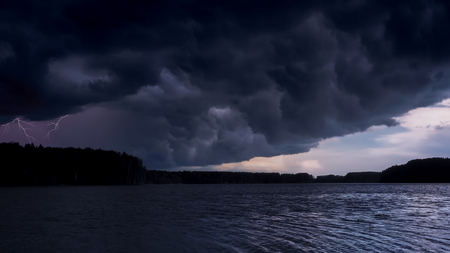 Thundercloud overshadows the sun. Stormy sky over the evening river lake. Dark clouds sky landscapeの写真素材