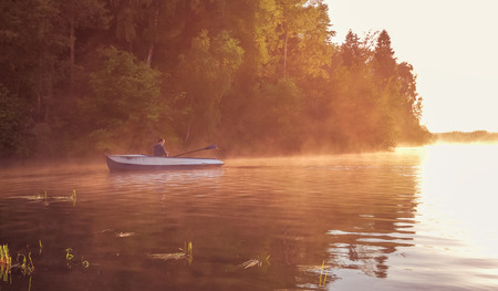 A young guy rides a boat on a lake during a golden sunset. Man rowing a boat in backlight of the...