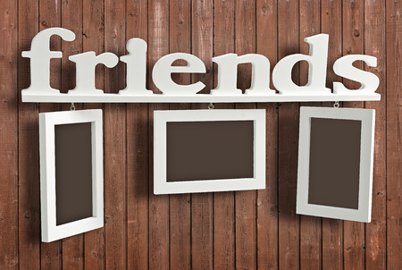 White wooden photo frame with text Friends on wooden wall. Hanging Photo Frame consists of three frames and the word Friends.の写真素材