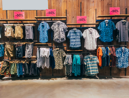 Row of colorful man apparel on shoulder hangers of at boutique in mall. Clothes hanging on rack. Set of casual male fashion on wooden hanger. Wardrobe showcase 50 percent discount.の写真素材
