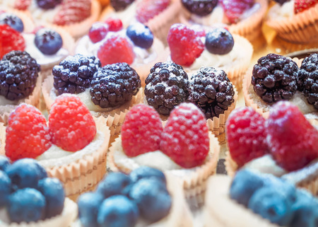 Many cakes with berries. Background of cupcakes with raspberries, blackberries and blueberries.の写真素材