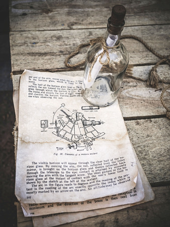 Vintage still life with sextant picture in a old book and empty glass bottle with rope on aged wooden background. The book describes the technique of sextant use in English. Sailing and travel concept top viewの写真素材