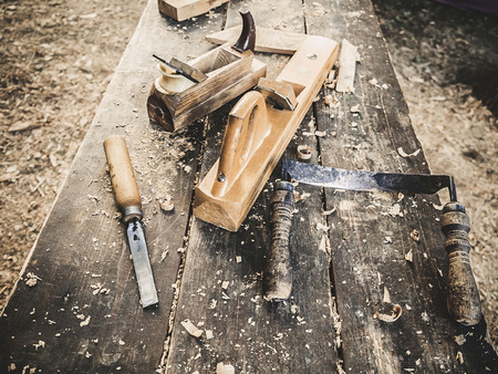 Old woodworking hand tool: wooden plane, chisel and drawing knife in a carpentry workshop on dirty rustic table covered with sawdust background side viewの写真素材