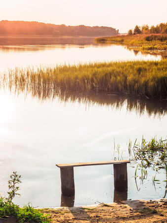 Empty bench near the river at sunset. Away from the hustle and bustle. Sun setting over the horizon. Forest near the Volga River. Beautiful natural backgroundの写真素材