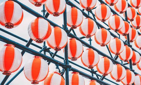 Many paper red-white oriental paper lanterns hanging in a row on blue sky backgroundの写真素材
